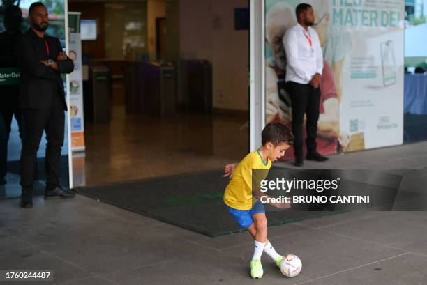 Child wearing the Brazilian national team t-shirt plays with a ball outisde the Mater Dei hospital, where Brazilian forward Neymar underwent surgery,...