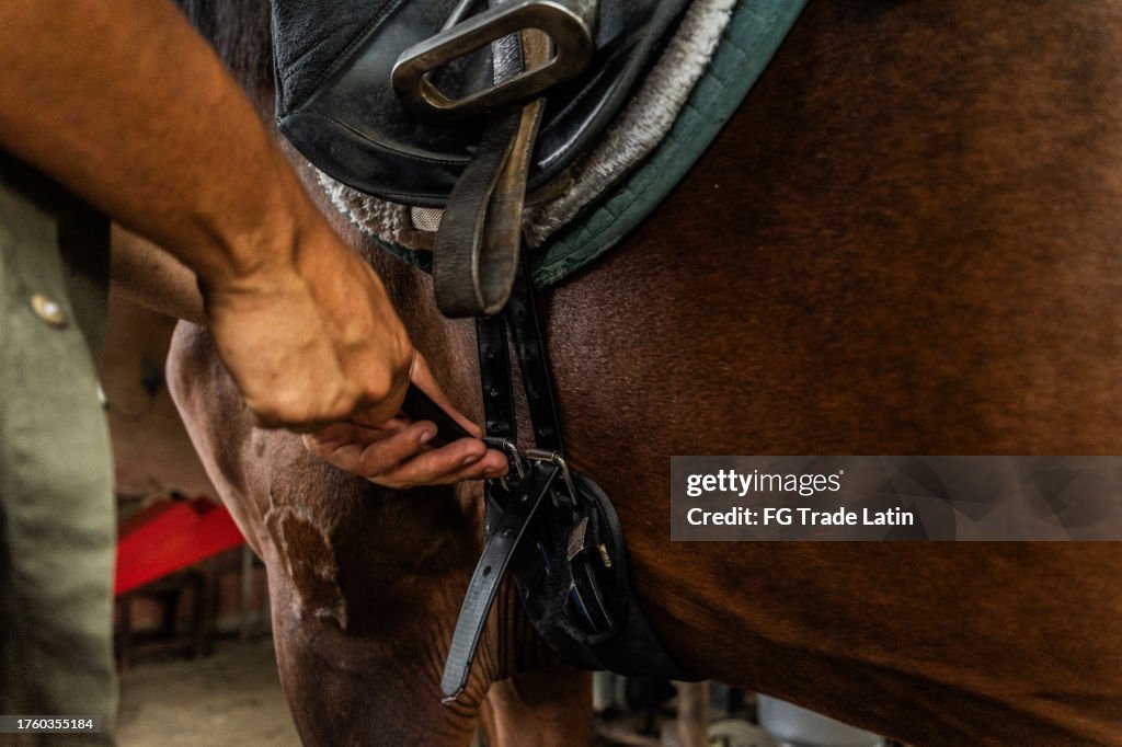 Close-up de um homem colocando uma sela em um cavalo