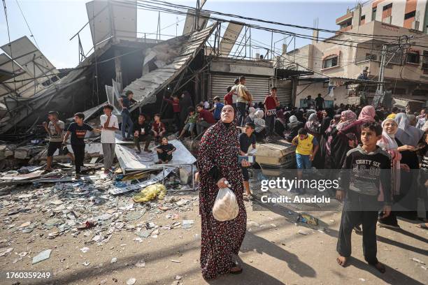 Civilians look up as Israeli airstrikes continue and wait in front of a partially collapsed, still operational bakehouse in Nuseirat refugee camp in...