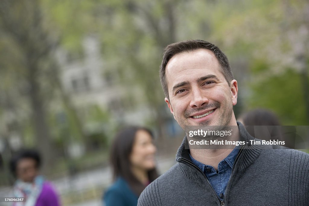 A group of people in a city park. A man in a grey sweater, smiling.