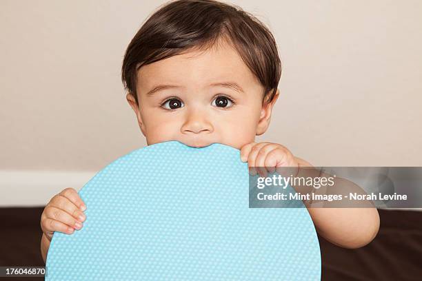 a young 8 month old baby boy wearing cloth diapers, holding a large blue disc and chewing the edge. - mastigar imagens e fotografias de stock