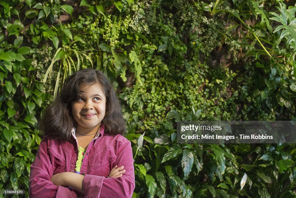 Outdoors in the city in spring. An urban lifestyle. A young girl standing in front of a wall covered with ferns and climbing plants.