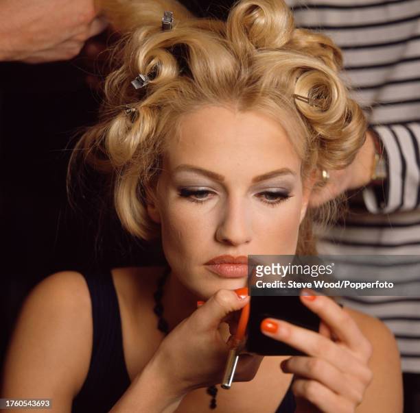 Dutch model Karen Mulder applying lipstick while having her hair styled backstage at a Chanel fashion show, circa 1995.