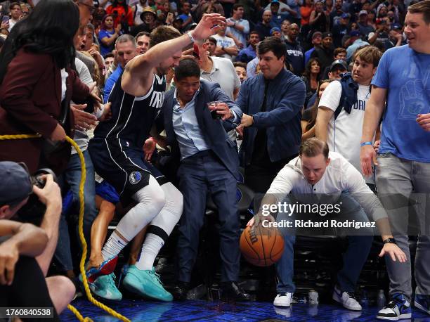 Luka Doncic of the Dallas Mavericks falls into fans trying to save a loose ball against the Brooklyn Nets in the fourth quarter at American Airlines...