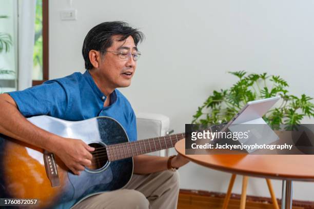 a portrait of a man sitting at home, playing guitar on his laptop, makes an excellent recording studio. - practice stock pictures, royalty-free photos & images