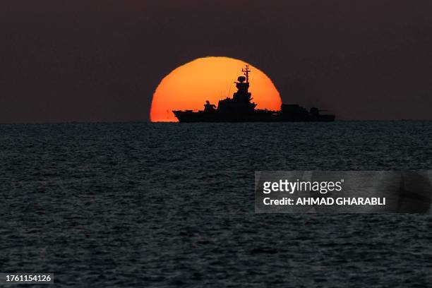 The sun sets behind a warship sailing the Mediterranean sea waters off the coast of Israel's northern city of Acre on November 3, 2023.