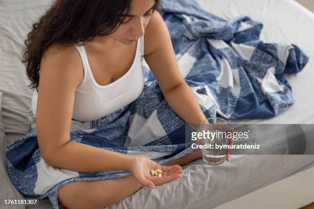 woman holding a pill in her hand on bed with glass of water. - medicare supplement stock pictures, royalty-free photos & images