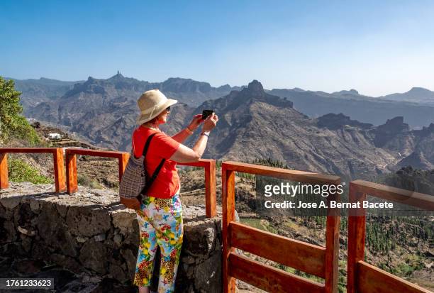 a tourist woman taking photos with her phone of a landscape from a viewpoint on the island of gran canaria. - artenara fotografías e imágenes de stock