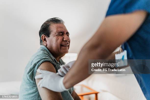 male nurse giving injection to a senior man patient at his house - infection prevention stockfoto's en -beelden