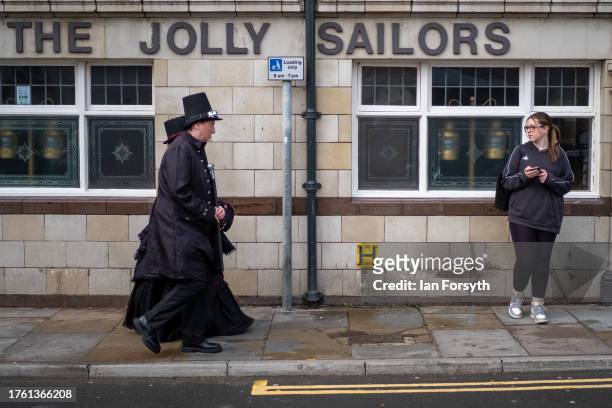 Couple wearing goth clothing walk through town as they attend Whitby Goth Weekend on October 28, 2023 in Whitby, England. The Whitby Goth Weekend is...