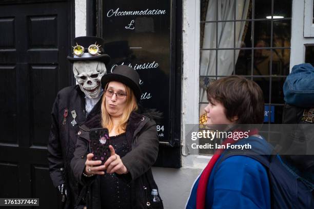 Woman takes a selfie with a man in a skull mask during Whitby Goth Weekend on October 28, 2023 in Whitby, England. The Whitby Goth Weekend is an...