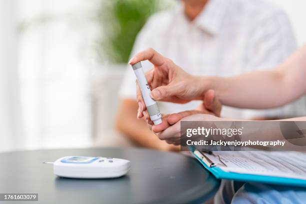 a nurse administers a blood sugar test to a patient at home. - administers stock pictures, royalty-free photos & images