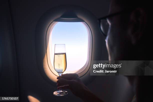 hand holding champagne glass against airplane window - passenger cabin stock pictures, royalty-free photos & images