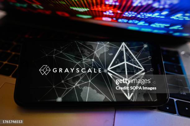 In this photo illustration, a GrayScale logo is displayed on a smartphone with stock market percentages on the background.