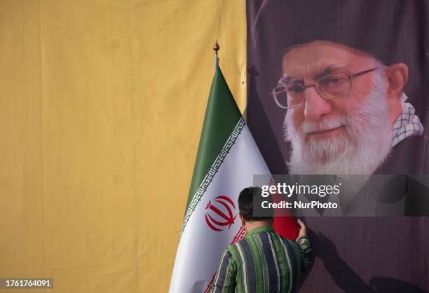 An Iranian man adjusts an Iranian flag next to a portrait of Iran's Supreme Leader, Ayatollah Ali Khamenei, before Lebanon's Hezbollah...