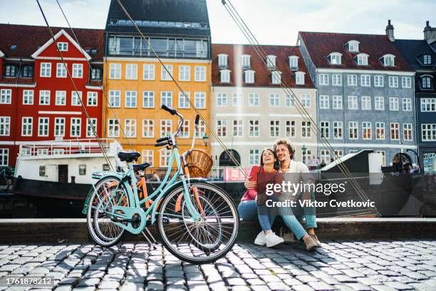 young romantic couple with their bicycles sitting by the stromma canal in copenhagen - toerist stockfoto's en -beelden