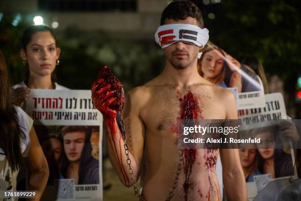 Man covered in fake blood holds a heart with a chain attached with the words "prisoner in gaza" written on him poses as part of an art installation...