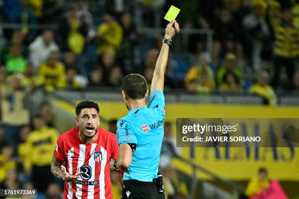 Spanish referee Mario Melero Lopez presents a yellow card to Atletico Madrid's Uruguayan defender Jose Gimenez during the Spanish league football...
