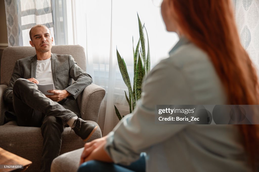 Stockfotografie Eine junge kaukasische Frau mit roten Haaren befindet sich in einer Therapiesitzung mit einem männlichen Psychologen und führt während einer Beratungssitzung eine Diskussion: Stockfoto