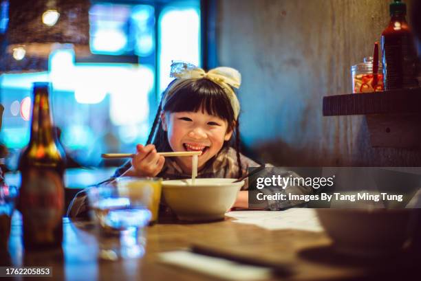 lovely cheerful girl smiling joyfully at the camera while enjoying meal in a japanese restaurant - chinese noodles stock pictures, royalty-free photos & images