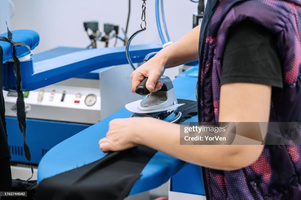 Worker in a tailoring factory ironing fabrics