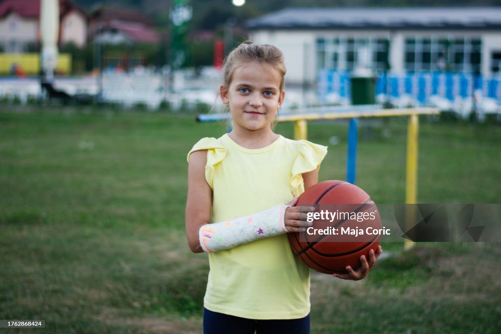 Liitle Mädchen mit gebrochenem Arm trägt orthopädischen Gips mit Baskeball