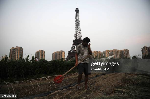 This picture taken on August 7, 2013 shows a resident farming with the background of a replica of the Effel Tower in Tianducheng, a luxury real...