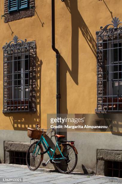 turquoise bicycle with a basket under a bright yellow wall in lucca - lucca italy stock pictures, royalty-free photos & images
