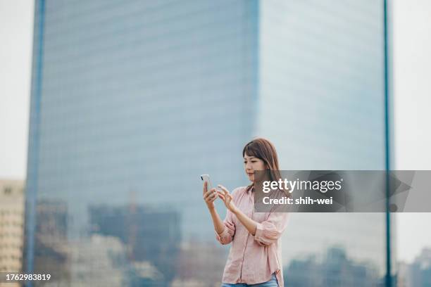 a young asian woman uses a smartphone in the city - convenience icon stock pictures, royalty-free photos & images