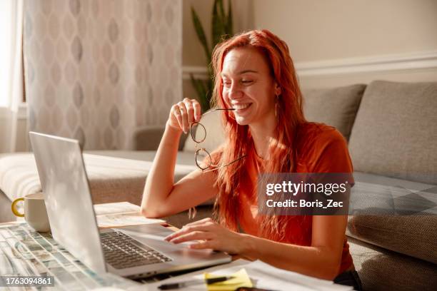 eine schöne junge frau mit roten haaren und brille arbeitet von zu hause aus, multitasking. sie denkt darüber nach, wie sie ein problem lösen kann. - social media marketing stock-fotos und bilder