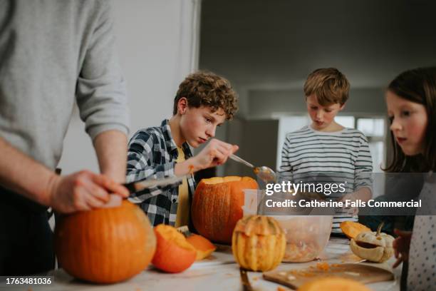 three children and an adult sit around a table in a domestic environment and make jack o' lanterns out of large pumpkins - kunst und handwerkserzeugnis stock-fotos und bilder