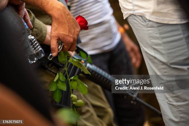 Person holds a flower near a soldier carrying a rifle during the funeral of Lili Itamari and Ram Itamari a couple from Kibbutz Kfar Aza who were...