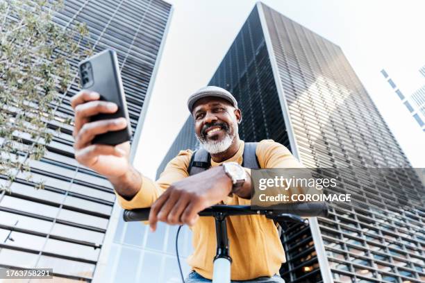 man on a bike looking at his phone in the city. man on a bike taking a selfie in the city - mature men office stock pictures, royalty-free photos & images