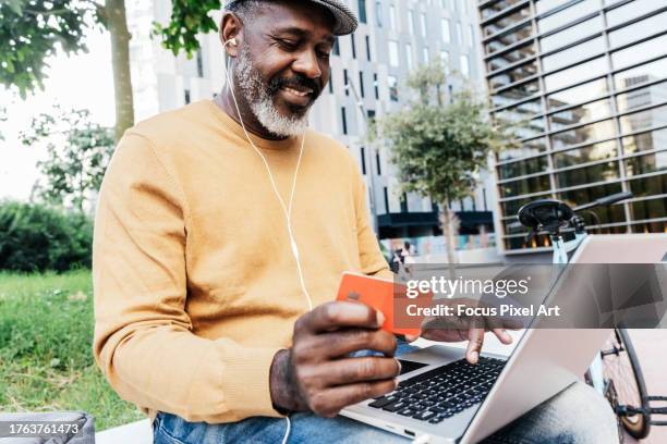 a person shopping online with a laptop and a credit card in a park - credit card art stock pictures, royalty-free photos & images