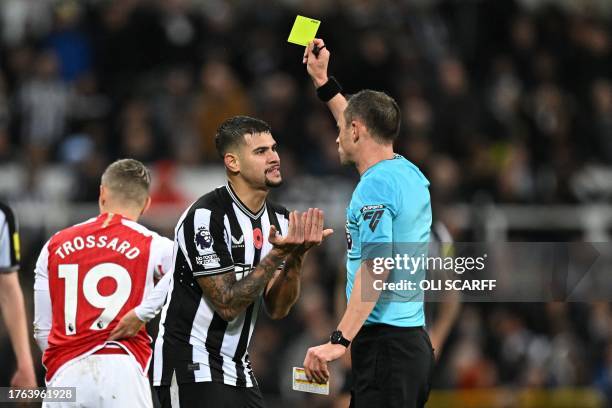 English referee Stuart Attwell shows a yellow card to Newcastle United's Brazilian midfielder Bruno Guimaraes during the English Premier League...