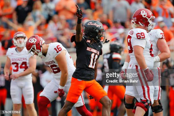 Cornerback Dylan Smith of the Oklahoma State Cowboys celebrates as tight end Blake Smith of the Oklahoma Sooners reacts after kicker Zach Schmit...
