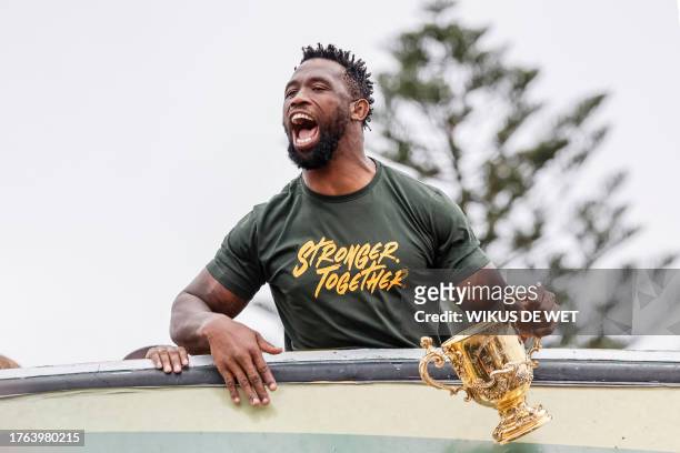 South Africa's flanker and captain Siya Kolisi reacts as he holds the throphy from the bus carrying the rest of the team during the Springboks...