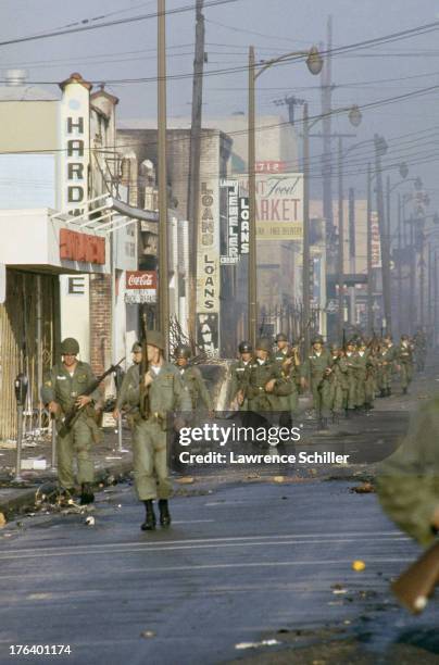 Line of National Guardsmen march past shuttered and burned-out businesses on a street in the Watts neighborhood after the declaration of Marshall Law...