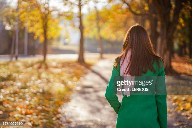 back view of a young woman walking in a city park - lerexis stockfoto's en -beelden