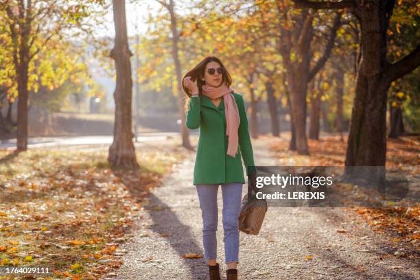 young happy woman walking on sidewalk in street fixing her hair - lerexis stockfoto's en -beelden