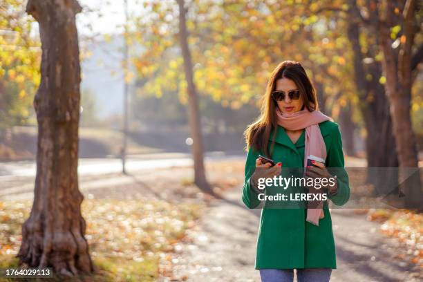 young business lady uses mobile phone while walking in city park - lerexis stock pictures, royalty-free photos & images