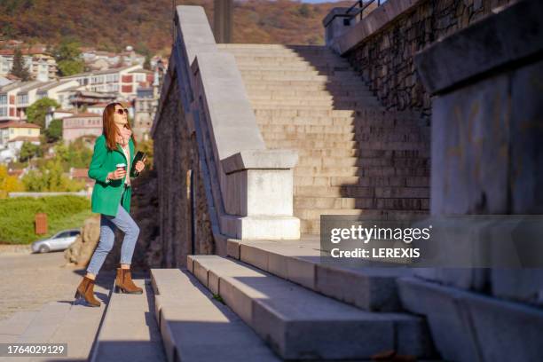 young woman climbing stairs of building in city park in autumn - lerexis stockfoto's en -beelden