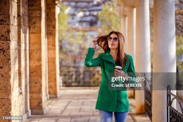 young woman walking in autumn public park with paper coffee cup - lerexis stockfoto's en -beelden