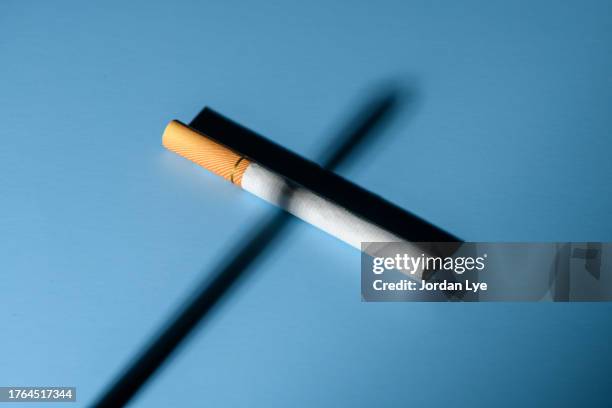 cigarette and shadow forming cross on blue background - antitabagismo imagens e fotografias de stock