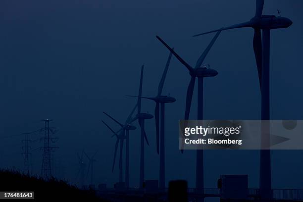 Wind turbines manufactured by Hitachi Ltd. Stand at night at an offshore wind farm operated by Wind Power Ibaraki Inc. In Kamisu, Ibaraki Prefecture,...