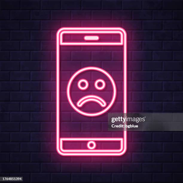 ilustrações, clipart, desenhos animados e ícones de smartphone com emoji triste. ícone de néon brilhante no fundo da parede de tijolo - disappointing phone