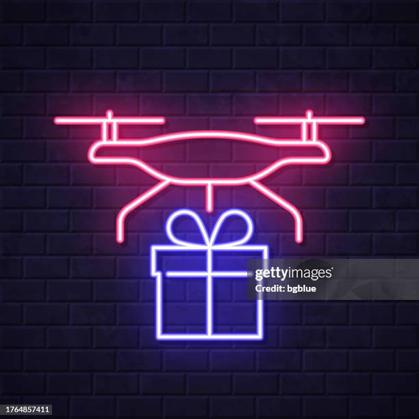 lieferdrohne mit geschenk. leuchtende neon-ikone auf backsteinwandhintergrund - flying drone stock-grafiken, -clipart, -cartoons und -symbole