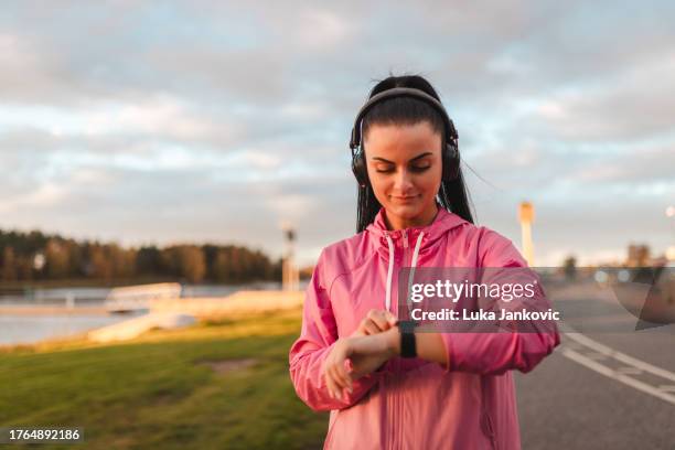 beautiful young female athlete checking her smartwatch while on a run outdoors - wireless headphones stock pictures, royalty-free photos & images