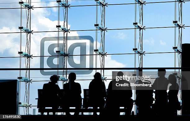 Passengers sit on a bench as the logo of Deutsche Bahn AG is displayed on the glass facade of Berlin Central Station, also known as Hauptbahnhof, in...