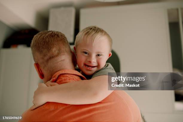 portrait of boy with down syndrome hugging father at home - down syndrome stock pictures, royalty-free photos & images